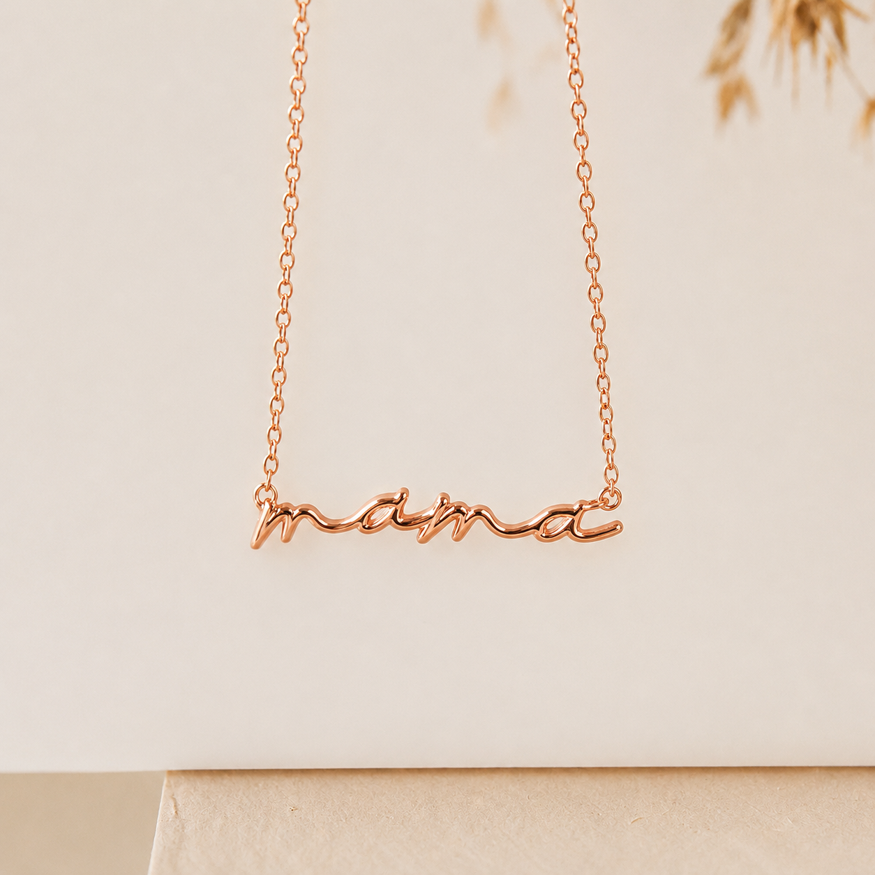 Rose gold 'mama' necklace on a beige background